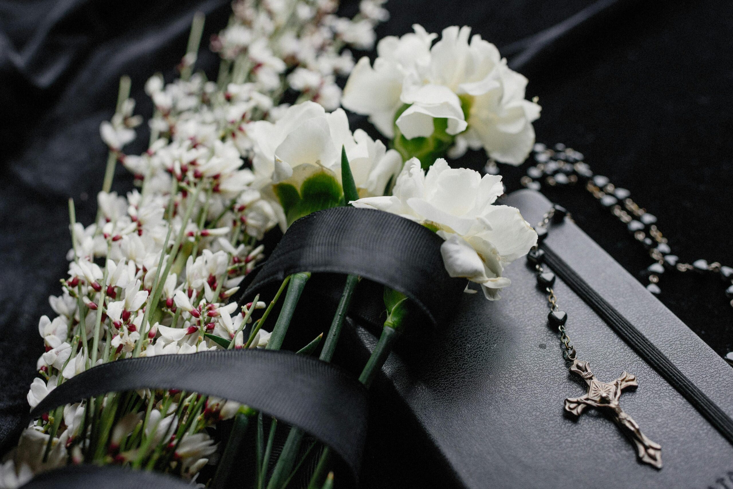 Cremation pre-planning Close-up of white flowers and rosary on dark cloth, symbolizing mourning and spirituality.
